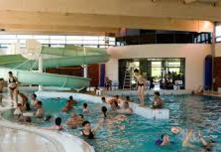 Indoor swimming pool with people and children enjoying the water, featuring a green waterslide at a holiday park.