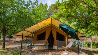 Ponza Safari-Zelt mit gelbem Vordach, Holzterrasse, Stühlen und grüner Natur ringsum.