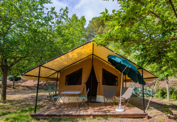Ponza Safari-Zelt mit gelbem Vordach, Holzterrasse, Stühlen und grüner Natur ringsum.