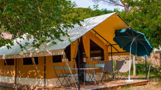 Safari Ponza Zelt mit Terrasse, Stühlen, Tisch und Sonnenschirm in natürlicher, grüner Umgebung.