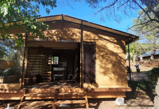 Glamping-Unterkunft mit Holzterrasse und Zelttuchwänden in einem bewaldeten Campingplatz.