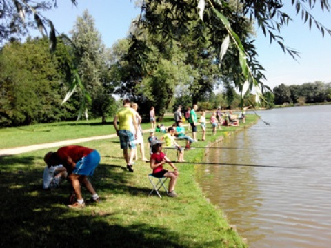 Holiday park in Auvergne-Rhône-Alpes, France, showing families and children fishing by a lake shore.