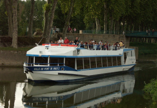 Tour boat carrying passengers cruises a narrow canal near Reyssouze in Auvergne-Rhône-Alpes, France.
