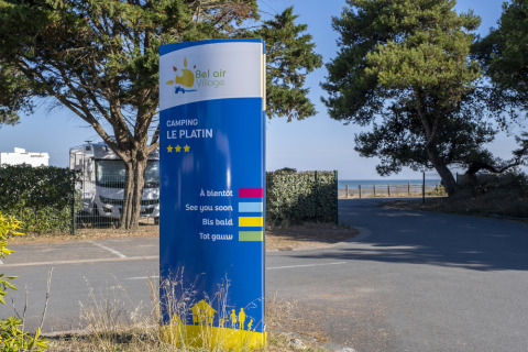 Entrance sign at Flower Camping Le Platin - La Redoute, a holiday park on Île de Ré, France, with trees and sea view.