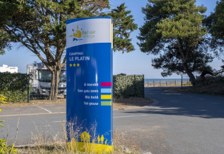 Indgangsskilt til Flower Camping Le Platin - La Redoute, feriepark på Île de Ré, Frankrig, med træer og udsigt til havet.