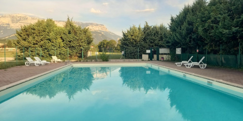 Outdoor swimming pool with lounge chairs, trees, and mountain views at Onlycamp Camping Chamarges, France.