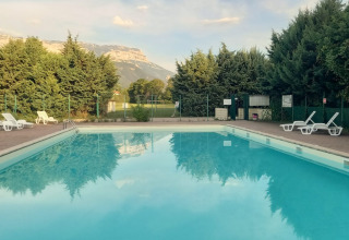 Outdoor swimming pool with lounge chairs, trees, and mountain views at Onlycamp Camping Chamarges, France.