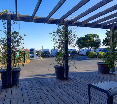 Blick von einer Holzterrasse auf einen Campingplatz mit Blumenkübeln und Wohnmobilen in Frankreich.