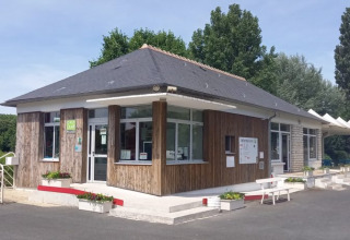 Indgangsområde ved Onlycamp Camping La Gâtine i Centre-Val de Loire, Frankrig, omgivet af træer og bænke.