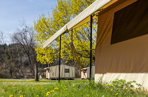 Buitenzicht op tenten en kleine hutten tussen het groen bij Onlycamp Camping Chamarges, Frankrijk.