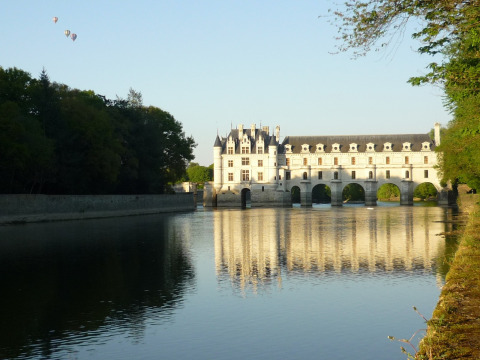 Photo d’un château enjambant une rivière en Centre-Val de Loire, avec montgolfières en arrière-plan.