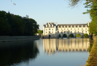Foto de un castillo junto a un río en Centre-Val de Loire, Francia, con globos aerostáticos en el cielo.