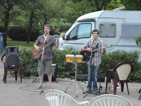 Zwei Musiker spielen Gitarre und singen mit Mikrofonen vor einem Wohnmobil im Onlycamp Camping de Besançon.