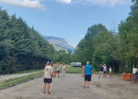 People play pétanque at Onlycamp Camping Chamarges, surrounded by greenery and mountains in France.