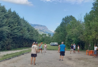People play pétanque at Onlycamp Camping Chamarges, surrounded by greenery and mountains in France.
