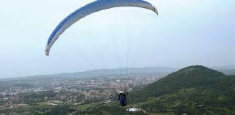 Een paraglider zweeft boven een groene heuvel en stad bij Onlycamp Camping de Besançon in Bourgogne-Franche-Comté, Frankrijk.