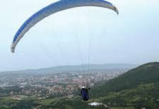 A paraglider soars above a scenic town and green hills at Onlycamp Camping de Besançon in Bourgogne-Franche-Comté, France.