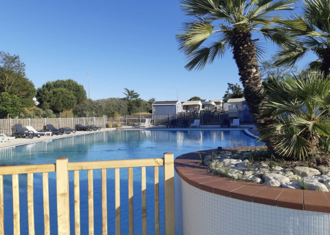 Freiluft-Swimmingpool mit Liegestühlen, Palmen und Bungalows im Flower Camping Le Platin - La Redoute, Île de France.