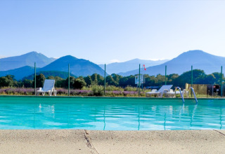 Outdoor swimming pool with lounge chairs, mountain views at Onlycamp Camping Chamarges in France.