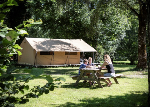 Famille assise à une table de pique-nique devant une tente safari Ponza, profitant d’un camping verdoyant.