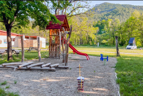 Playground with slide and wooden climbing structures at Onlycamp Camping Chamarges, surrounded by nature.