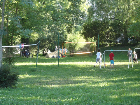 Children play football and badminton on a grassy campsite surrounded by trees at Onlycamp Camping de Besançon.