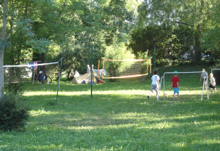 Niños juegan al fútbol y bádminton en un camping verde rodeado de árboles en Onlycamp Camping de Besançon.