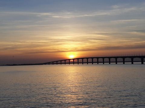 Mooie zonsondergang boven het water met een lange brug bij Rivedoux-Plage, Île de Ré, Frankrijk, op de achtergrond.