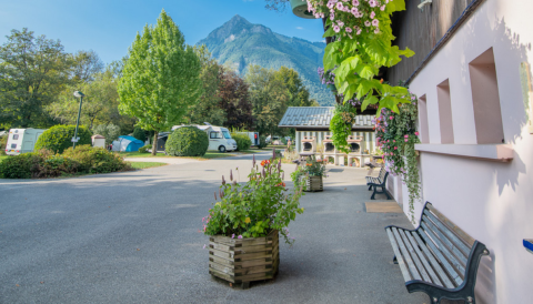 Rustig beeld van Onlycamp Camping Les Thézières met bergen, groen, banken en hangende bloemenmanden.