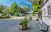 Scenic view of Onlycamp Camping Les Thézières with mountain backdrop, greenery, benches, and flower boxes.