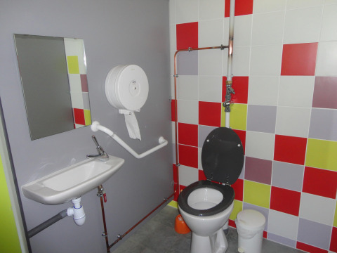 Baño accesible con inodoro, lavabo, espejo y azulejos de colores en Onlycamp Camping de Besançon, Francia.