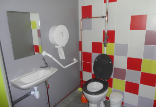 Toegankelijke badkamer met toilet, wastafel, spiegel en kleurrijke tegels bij Onlycamp Camping de Besançon, Frankrijk.