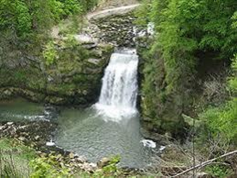 Kleine waterval omringd door groene bomen bij Onlycamp Camping de Besançon in Bourgogne-Franche-Comté, Frankrijk.