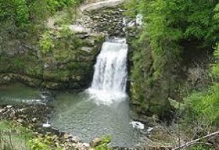 Kleine waterval omringd door groene bomen bij Onlycamp Camping de Besançon in Bourgogne-Franche-Comté, Frankrijk.