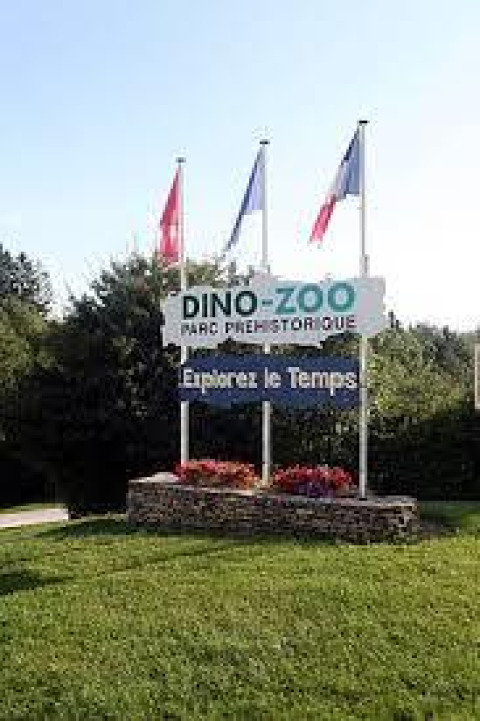Cartel de entrada al Dino-Zoo, parque prehistórico con flores y banderas en Bourgogne-Franche-Comté, Francia.