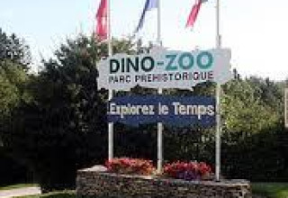 Eingangsschild des Dino-Zoos mit Blumenbeeten und französischen Flaggen in Bourgogne-Franche-Comté, Frankreich.