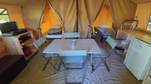 Innenraum eines Glamping-Zeltes mit Esstisch, Stühlen, Kochnische, Kühlschrank und Betten.