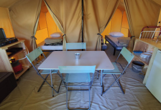 Interior of a glamping tent featuring a dining table, chairs, kitchenette, fridge, and two beds.
