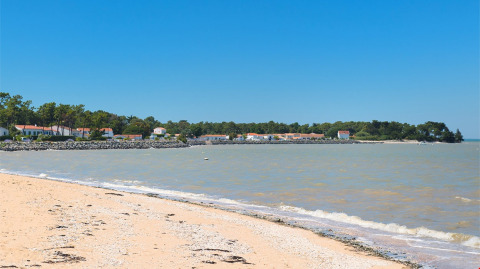 Sandy beach with gentle waves and holiday lodges seen at Flower Camping Le Platin - La Redoute, Île de France, France.