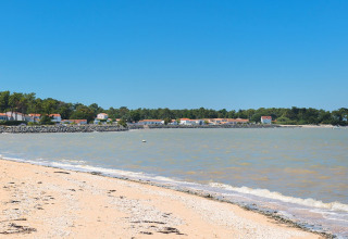 Sandy beach with gentle waves and holiday lodges seen at Flower Camping Le Platin - La Redoute, Île de France, France.