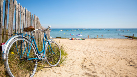 Blauwe fiets tegen houten hek op zandstrand bij Flower Camping Le Platin - La Redoute, Île de France.