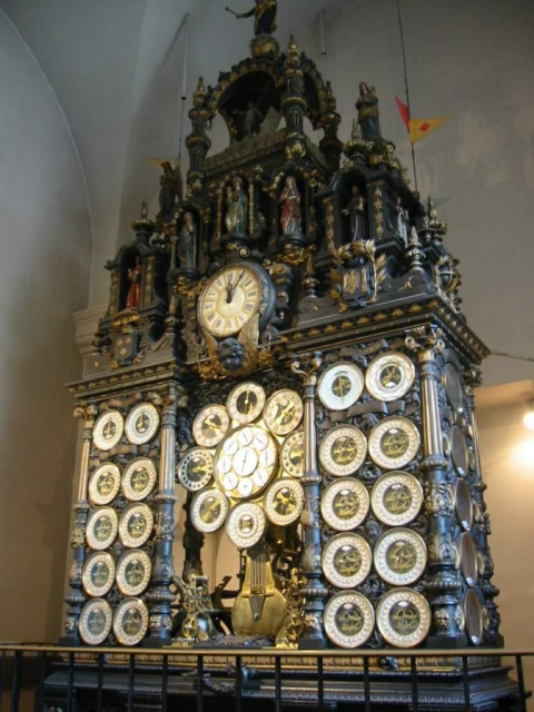 Ancient astronomical clock with multiple dials and ornate statues on display inside a historic building.