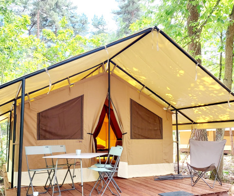 Hébergement glamping sous tente spacieuse avec terrasse, table et chaises, entouré de forêt.