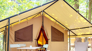 Tenda glamping spaziosa con veranda, tavolo e sedie, immersa in una lussureggiante foresta verde.