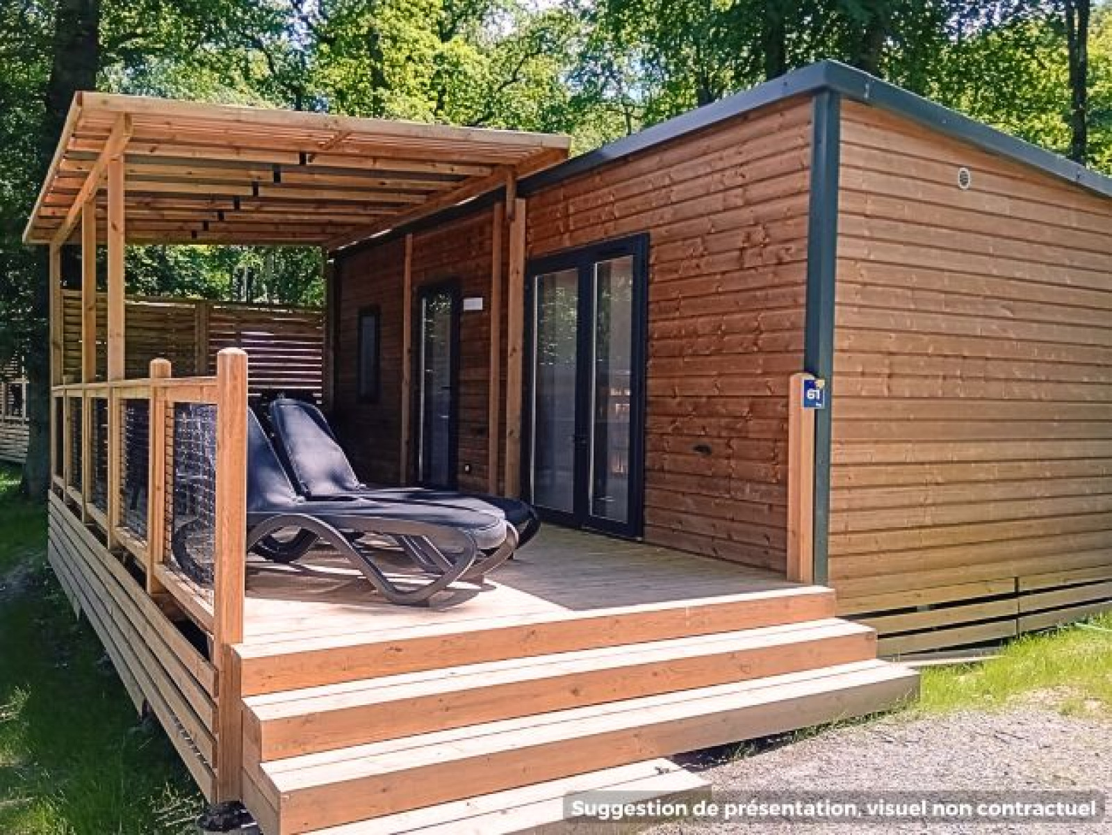 Een moderne houten lodge met overdekt terras en ligstoelen, omgeven door bomen in een bosrijke omgeving.