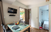 Dining area inside a lodge, with a set table, wall-mounted TV, and view into a cozy bedroom.