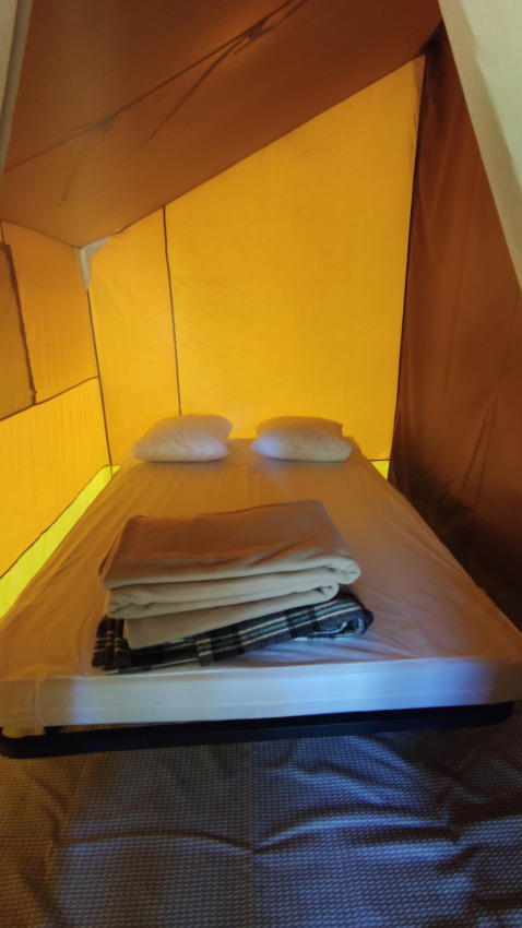 Intérieur d'une tente glamping avec lit, deux oreillers et couvertures dans une ambiance chaleureuse.