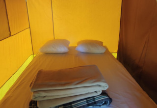 Interior de tienda glamping con cama, dos almohadas y mantas dobladas en un ambiente cálido.