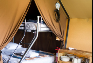 Vue intérieure d'une tente glamping avec lits superposés, petite cuisine et étagère avec vaisselle.