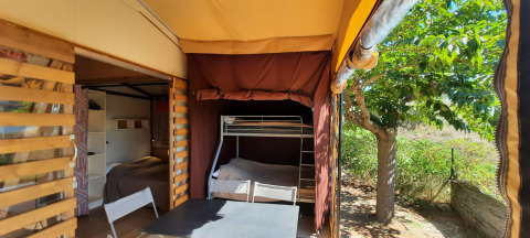 Glamping-Unterkunft mit Etagenbett, Tisch und Stühlen unter Zeltplane, Baum und Natur draußen.